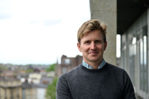 University of Bristol alumnus Rupert Baker stands on a balcony with Bristol in the background.